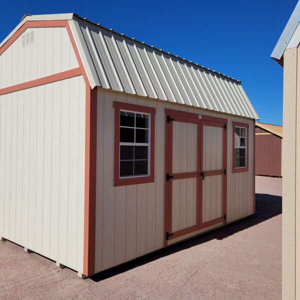 Barn style storage shed with double doors and two windows. Tan metal roof and walls with red trim.