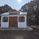 Front view of 12x16 Studio Gable in Cotopaxi, CO with three windows and double doors, wood trim with white walls.