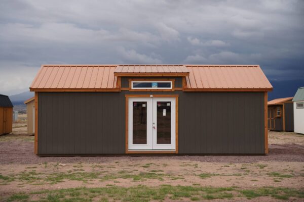 Front view of a large Studio Gable 12x28 storage shed with residential-style double doors, grey wood siding, and a metal roof.