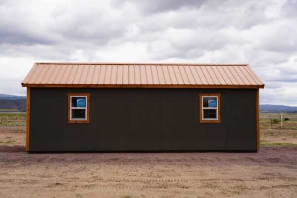 Back view of a large Studio Gable 12x28 storage shed with grey wood siding and a metal roof.