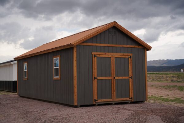 Studio Gable 12x28 storage shed viewed from the back corner, showing double swinging doors, grey wood siding, and two windows.