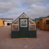 Front view of an 8x12 Green House with wood frame, green metal siding and roof, and plastic covering on the upper walls, highlighting the door in the front.