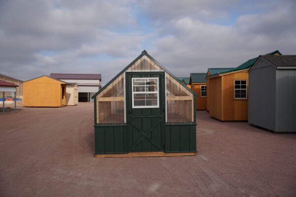 Front view of an 8x12 Green House with wood frame, green metal siding and roof, and plastic covering on the upper walls, highlighting the door in the front.