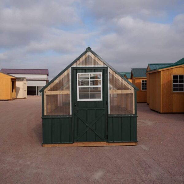 Front view of an 8x12 Green House with wood frame, green metal siding and roof, and plastic covering on the upper walls, highlighting the door in the front.