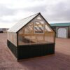 Back view of an 8x12 Green House with wood frame, green metal siding and roof, and plastic covering on the upper walls, highlighting the window in the back.