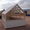 Back view of an 8x12 Green House with wood frame, metal siding and roof, and plastic covering on the upper walls.
