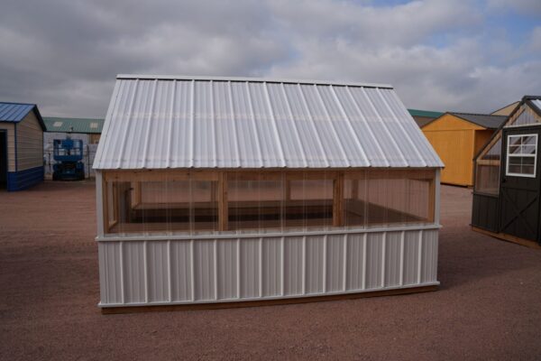 Side view of an 8x12 Green House with wood frame, metal siding and roof, and plastic covering on the upper walls.