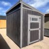 The sky is dotted with clouds as a 8x12 Urban Style storage shed with an angled roof stands tall, displaying the side marked by a grand door.