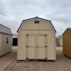 The sky is dotted with clouds as a shed and a house with a door stand on the outdoor property.