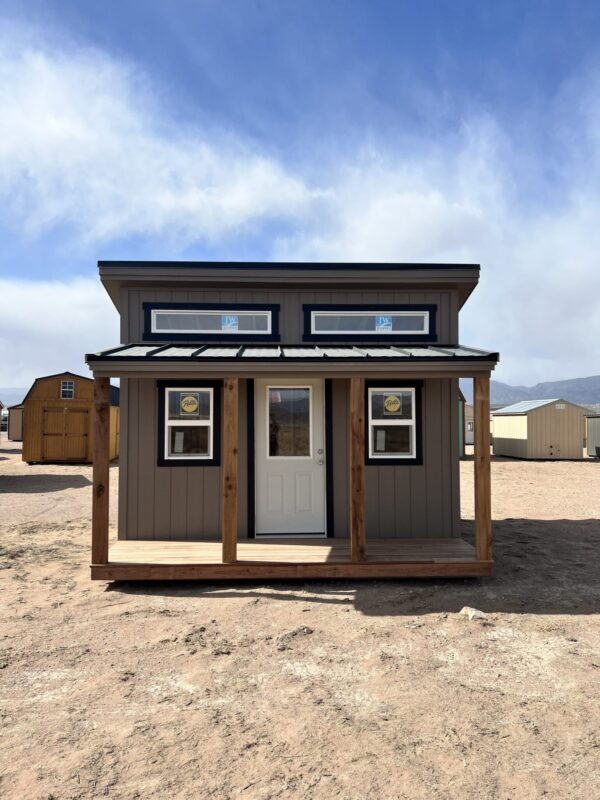 Behold the captivating sight of our 14x14 Outpost Style storage shed, viewed from the front, with its charming wooden porch and a backdrop of other sheds, creating a picturesque scene that epitomizes both functionality and aesthetics.