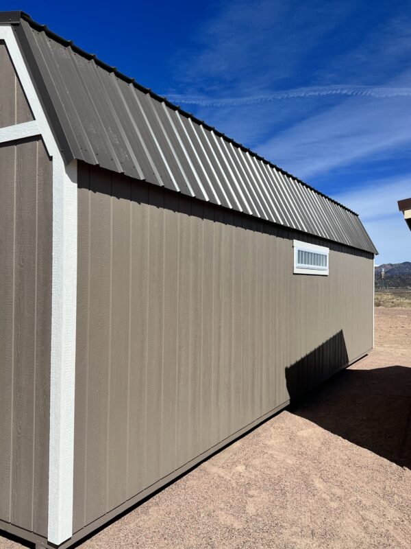 Experience the grandeur of our 14x32 Barn Style storage shed, as you view it from the corner and witness its impressive size. Adorned with beige wooden siding and a striking dark grey roof, this shed combines elegance and functionality on a large scale, offering abundant space for all your storage needs while enhancing the aesthetics of your property.