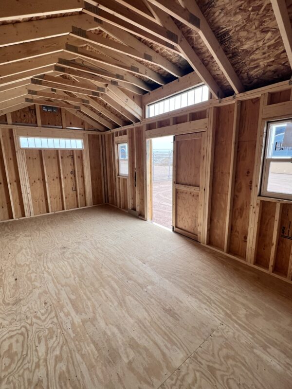 A wooden beam is being held up by a hardwood plank in an indoor property, with plywood ceiling, building insulation, wood flooring, attic, and window visible.