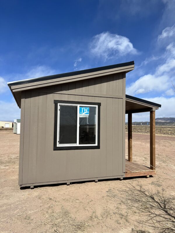 A side view of the spacious 14x14 Outpost Style storage shed, complete with a welcoming wooden porch and a large window.