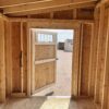 A view of the 8x12 Urban Style storage shed from the inside, showing the open single swinging door. The ceiling is made of a combination of wooden planks and plywood.