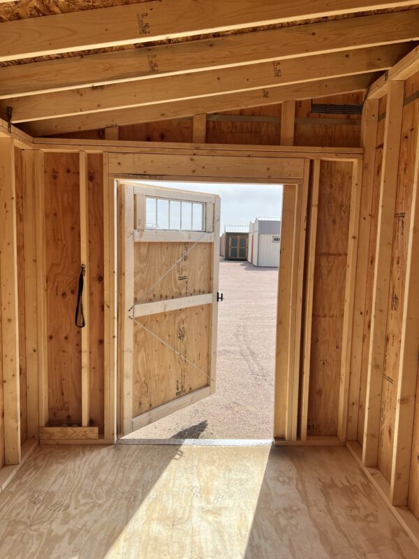 A view of the 8x12 Urban Style storage shed from the inside, showing the open single swinging door. The ceiling is made of a combination of wooden planks and plywood.