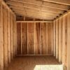 A view of the inside of the 8x12 Urban Style storage shed with a plywood ceiling and floor, wooden beams, and lumber supports.