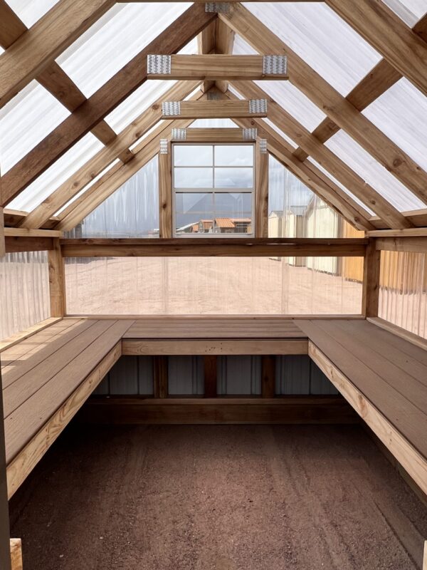 A beam of daylighting illuminates the wooden architecture of the indoor property, highlighting the lumber fixtures, roof, and ceiling of the 8x8 Greenhouse.