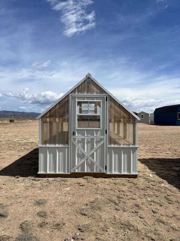 A view of the 8x12 Greenhouse from the front. In the background are other storage sheds and clouds in the sky above the property.