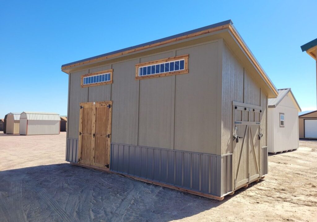 Large Royal Gorge style storage shed viewed from the front with double doors and ramp door on the side. Grey wooden walls with two wide short windows at the top.