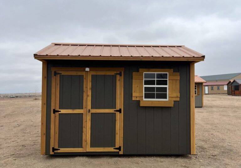 The sun shines through a window of a beach house, illuminating a sandy property with a shed and a building surrounded by a cloud-filled sky.