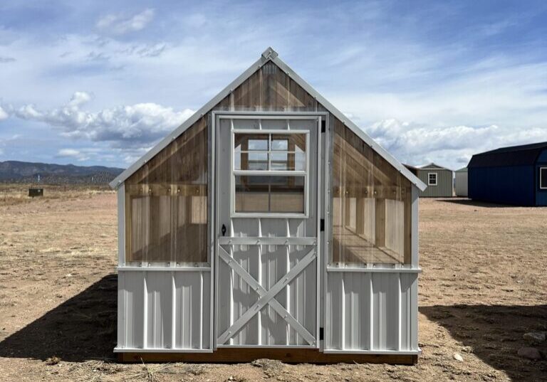 A view of the 8x12 Greenhouse from the front. In the background are other storage sheds and clouds in the sky above the property.